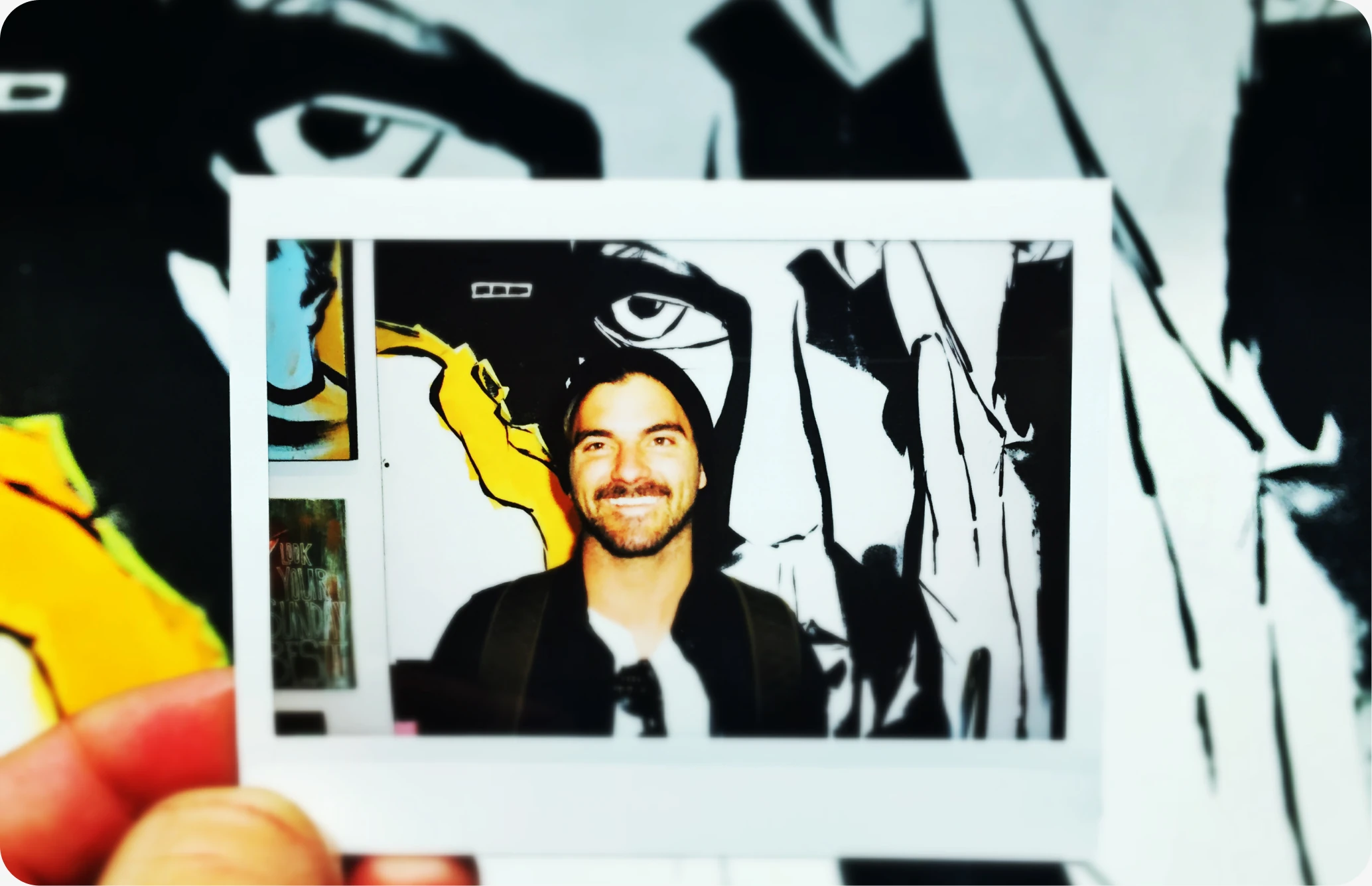 A photo of a photo of Eric, held up against a graphic mural