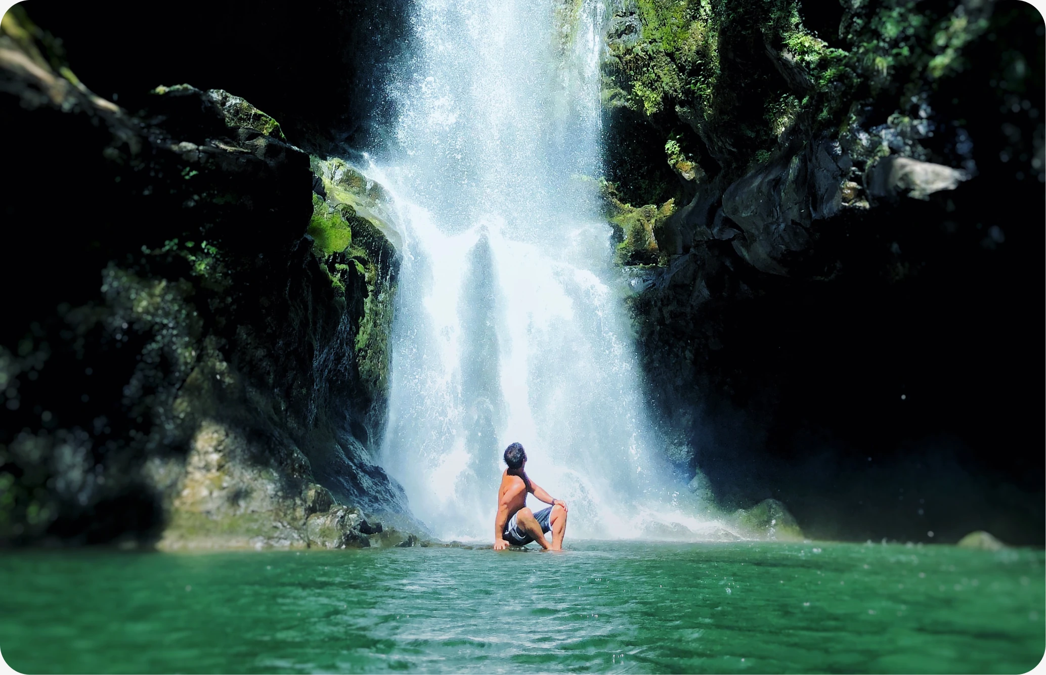 A waterfall pouring into a green pool, with a swimmer below